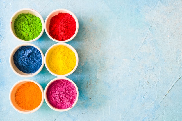 Polvere colorata di colore holi all&#39;interno delle ciotole bianche su sfondo blu dipinto