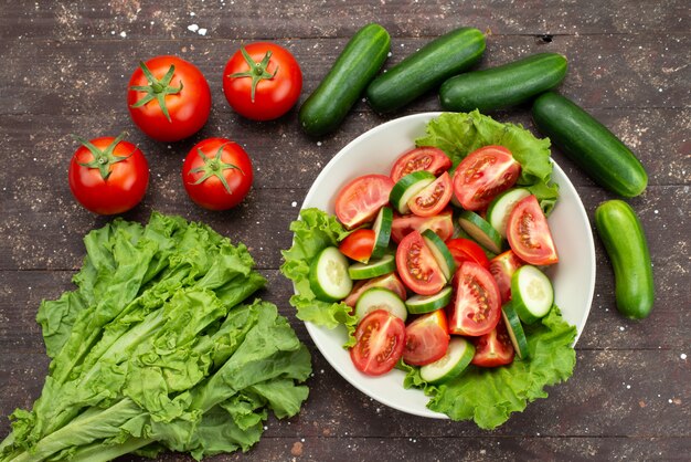 Pomodori affettati vista superiore con i cetrioli dentro il piatto bianco con insalata verde su marrone, insalata fresca di verdure dell'alimento