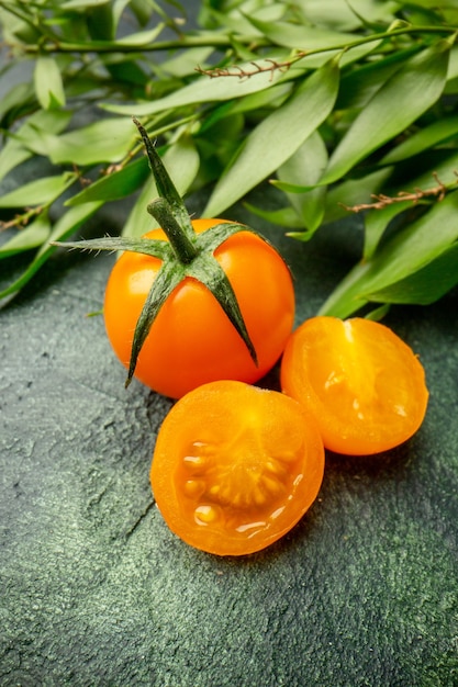 Pomodori arancioni vista frontale con foglie verdi su superficie verde scuro