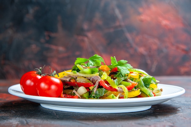 Pomodori ciliegia di insalata di verdure di vista frontale sul piatto ovale sulla superficie isolata rosso scuro