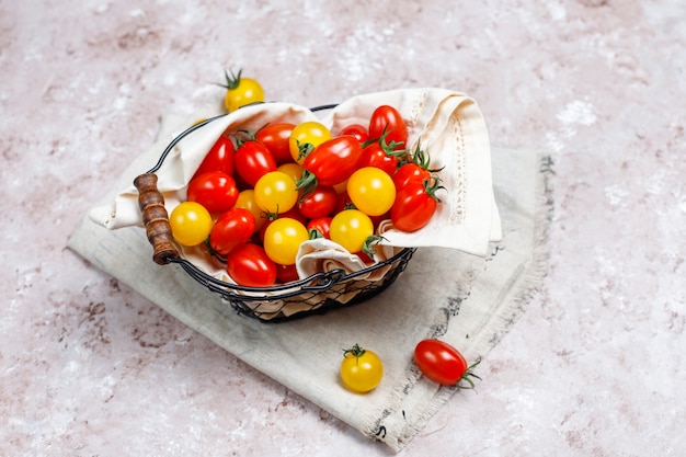 Pomodori ciliegia di vari colori, pomodori ciliegia gialli e rossi in un canestro su fondo leggero