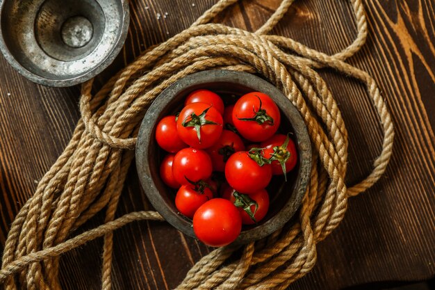 Pomodori ciliegia di vista superiore in una ciotola di legno con la corda sul tavolo