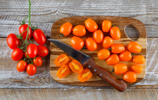 Pomodori con il coltello sul tagliere di legno e, disposizione piana.