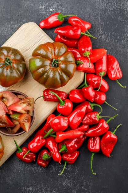 Pomodori di Kumato con le fette, vista superiore dei peperoni sulla parete grigia e del tagliere