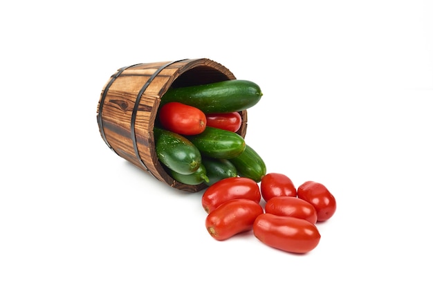 Pomodori e cetrioli da un secchio di legno sul bianco.