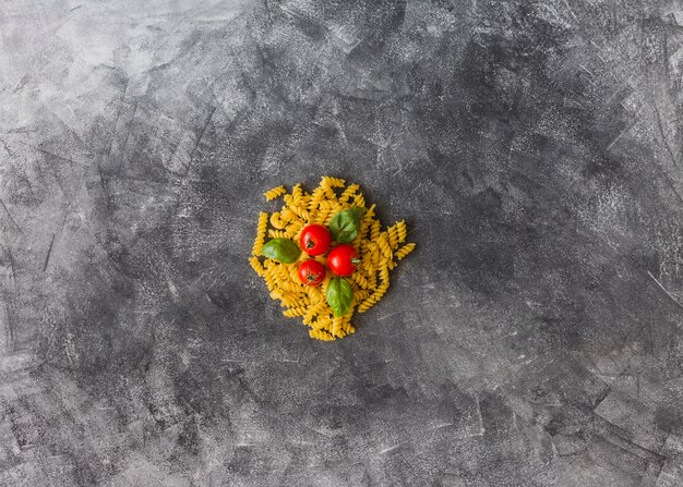 Pomodori e foglie di basilico sopra il fusilli crudo su sfondo macchia sporca