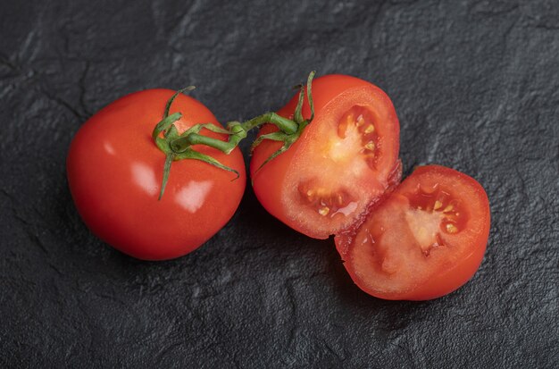 Pomodori freschi biologici. Pomodori interi o tagliati a metà su sfondo nero.