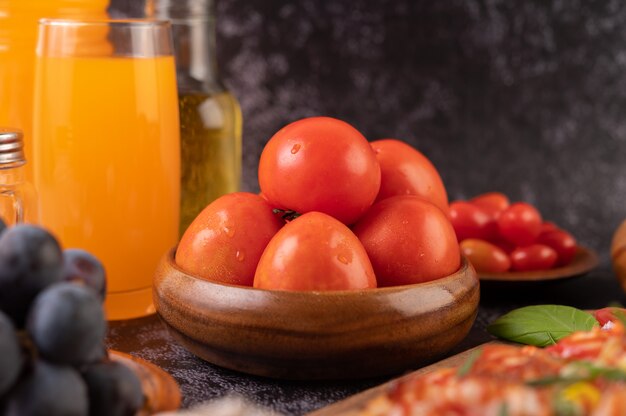 Pomodori freschi in una tazza di legno, uva e succo d'arancia in un bicchiere.