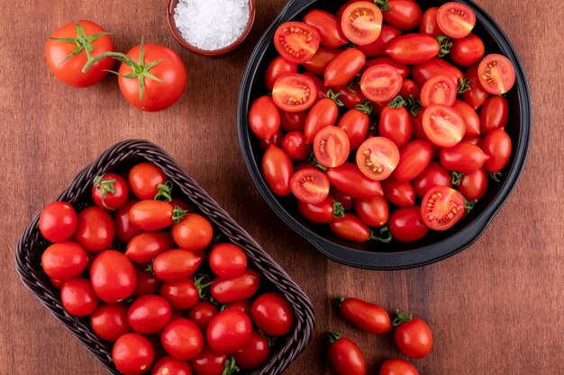 Pomodori in ciotola nera e nel cestino pomodoro ciliegia e sale in ciotola ceramica sulla superficie marrone della pietra