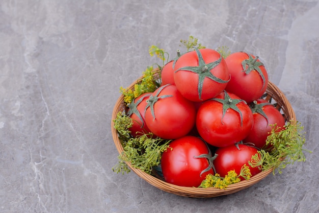 Pomodori in una tazza di legno con erbe intorno.