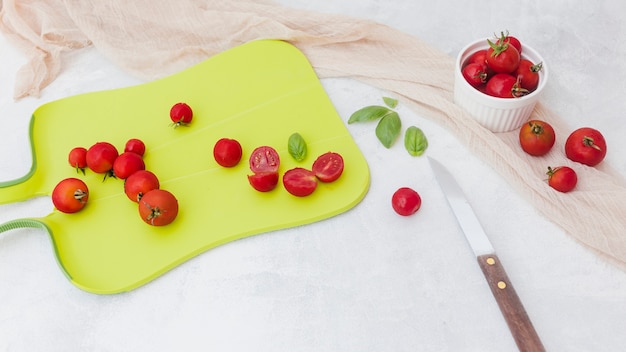 Pomodori rossi con basilico sul tagliere con coltello e sciarpa su sfondo bianco
