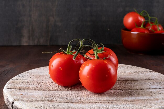 Pomodori rossi con gocce d'acqua e foglie di basilico fresco su un tagliere di legno alimenti biologici