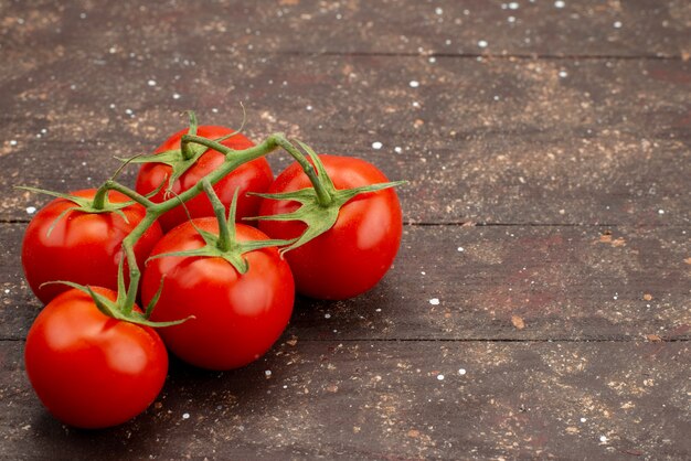 Pomodori rossi freschi di vista ravvicinata anteriore maturi e interi sul colore alimentare vegetale di sfondo marrone in legno