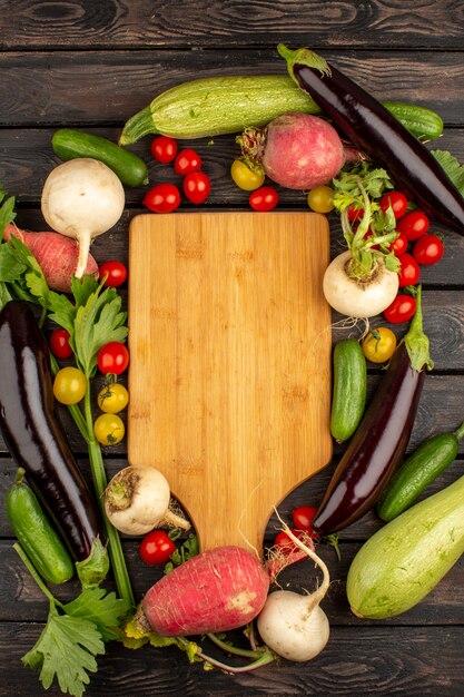 Pomodori rossi freschi e maturi altre verdure come ravanello rosso e melanzane nere su un pavimento di legno rustico