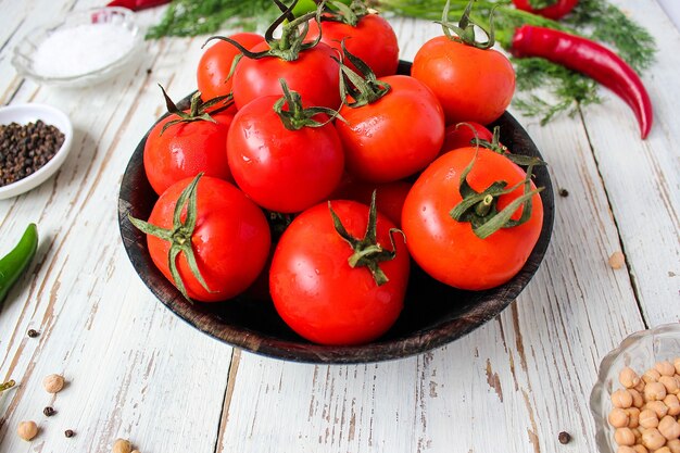 Pomodori rossi organici freschi in banda nera sul tavolo di legno bianco con verde e rosso e peperoncino, peperoni verdi, grani di pepe neri, sale, primi piani, concetto sano