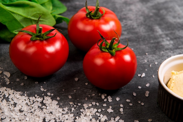 Pomodori, sale e verdure su superficie di legno grigio