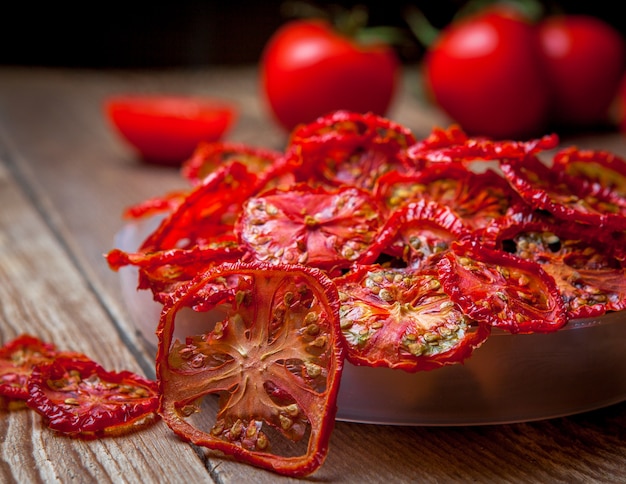 Pomodori secchi primo piano di vista laterale in piatto e pomodori freschi sulla tavola di legno