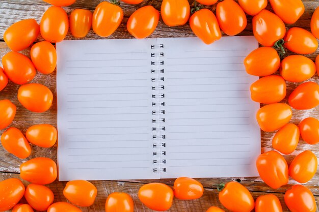 Pomodori sparsi con il quaderno aperto sulla tavola di legno, disposizione piana.