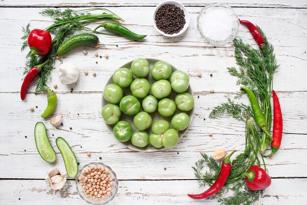 Pomodori verdi, sottaceti sul tavolo di legno bianco con verde e rosso e peperoncino, finocchio, sale, grani di pepe neri, aglio, pisello, da vicino, concetto sano, vista dall'alto, piatto