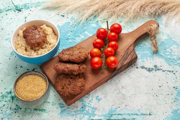 Pomodorini rossi vista frontale con cotolette di carne su farina di carne vegetale superficie blu