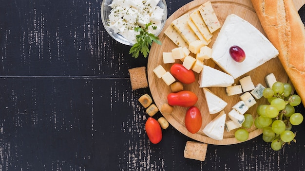 Pomodorini, uva, blocchi di formaggio e baguette sul tagliere rotondo sullo sfondo con texture