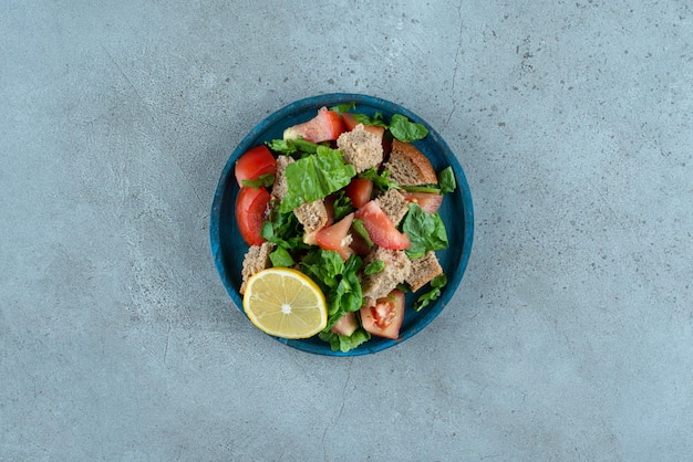 Pomodoro affettato, pane, limone e verdure sul piatto blu.