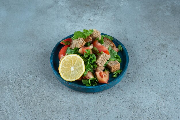 Pomodoro affettato, pane, limone e verdure sul piatto blu.