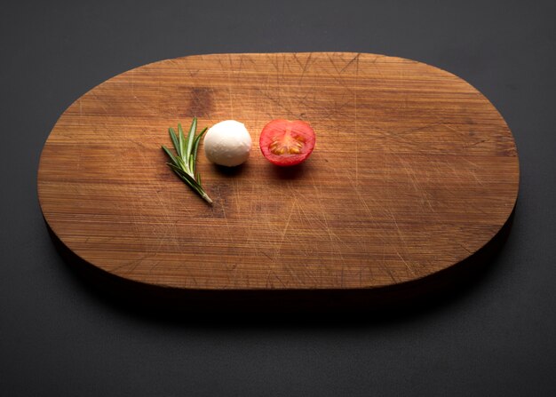 Pomodoro; rosmarino e formaggio sul tagliere di legno su sfondo nero