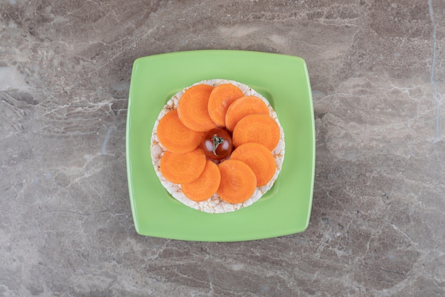 Pomodoro rosso al centro delle fette di carota e torta di riso sotto sul piatto, sulla superficie di marmo