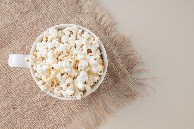 Popcorn classici bianchi in una tazza bianca su un pezzo di tela da imballaggio.