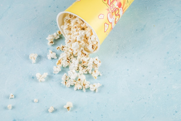 Popcorn da un contenitore giallo sul tavolo blu