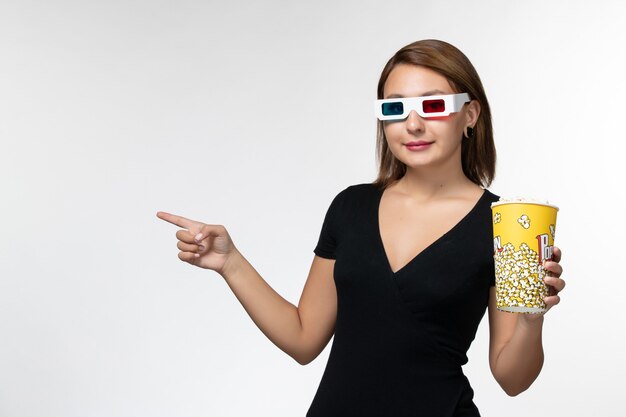 Popcorn della holding della giovane femmina di vista frontale in occhiali da sole d su superficie bianca
