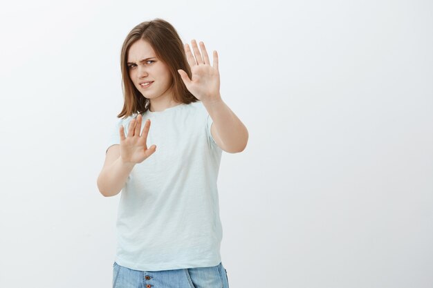 Portalo via da me. Ritratto di donna europea carina dispiaciuta e irritata intensa in t-shirt alla moda che copre il viso con le braccia tirate che si allontana con sguardo dispiaciuto essendo accecato dalla torcia