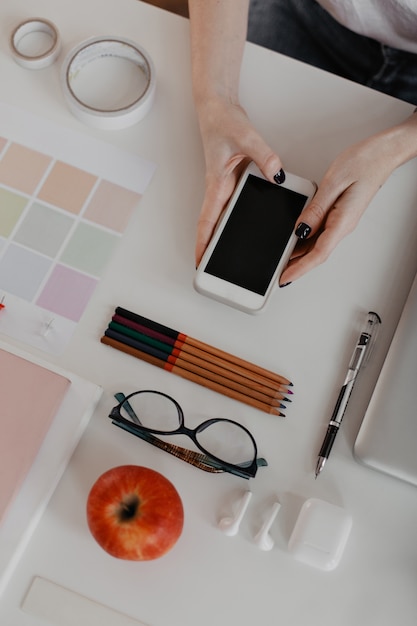 portraitgraph di cancelleria per ufficio su mani bianche e femminili con manicure nera, tenendo lo smartphone.