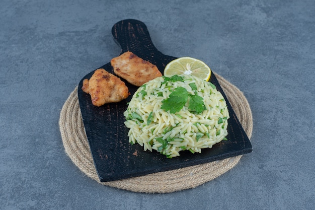 Porzione di riso con bocconcini di pollo su tavola nera.