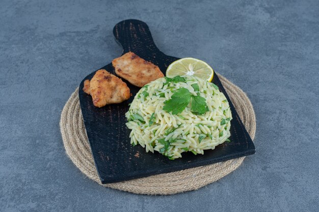 Porzione di riso con bocconcini di pollo su tavola nera.