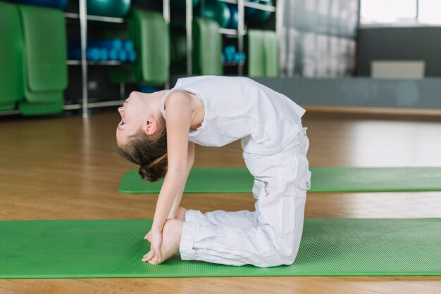 Posa di pratica del cammello del bello bambino della ragazza in palestra