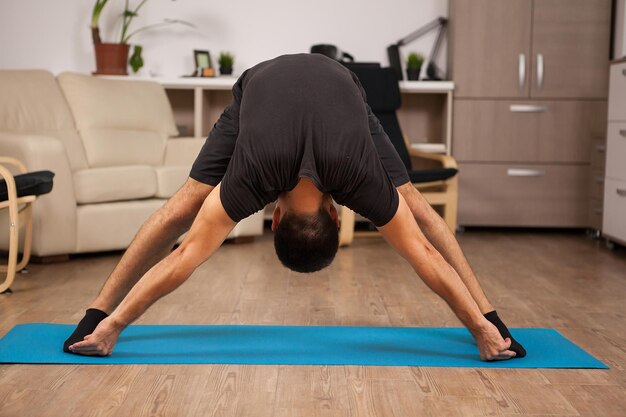 Posa yoga in piedi in avanti fatta da un adulto in forma sul pavimento di casa sua. Allenamento avvincente.