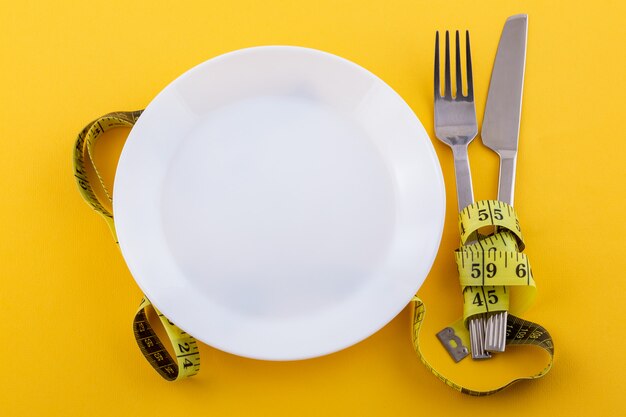 Posate e un piatto bianco con nastro di misurazione su un giallo, il concetto di perdita di peso e dieta