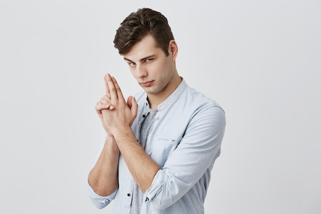 Positivo divertirsi maschio caucasico con capelli scuri e occhi azzurri, sopracciglio sollevato, fare facce, guardare seriamente, gesticolando fingendo di avere la pistola. Concetto di divertimento e gioventù