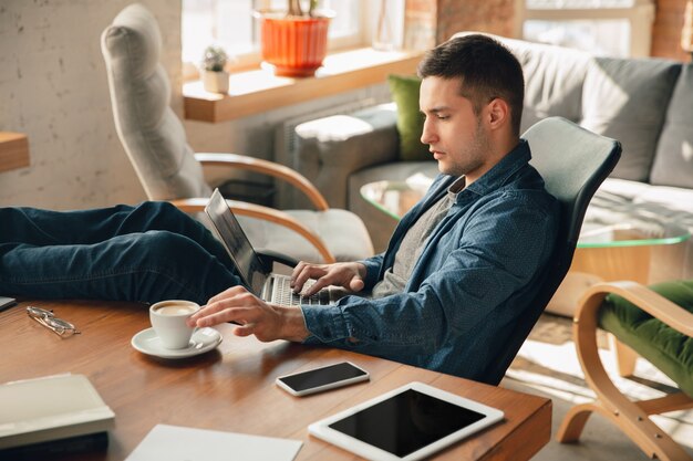 Posto di lavoro creativo: spazio di lavoro organizzato come preferisci per l'ispirazione. Uomo che lavora in ufficio in abbigliamento comodo, posizione rilassata e tavolo disordinato. Scegli l'atmosfera che desideri - ideale chiaro o caos.