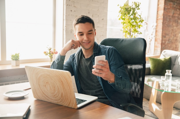 Posto di lavoro creativo: spazio di lavoro organizzato come preferisci per l'ispirazione. Uomo che lavora in ufficio in abbigliamento comodo, posizione rilassata e tavolo disordinato. Scegli l'atmosfera che desideri - ideale chiaro o caos.