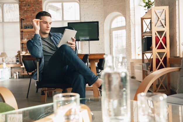 Posto di lavoro creativo: spazio di lavoro organizzato come preferisci per l'ispirazione. Uomo che lavora in ufficio in abbigliamento comodo, posizione rilassata e tavolo disordinato. Scegli l'atmosfera che desideri - ideale chiaro o caos.