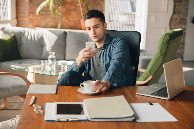 Posto di lavoro creativo: spazio di lavoro organizzato come preferisci per l'ispirazione. Uomo che lavora in ufficio in abbigliamento comodo, posizione rilassata e tavolo disordinato. Scegli l'atmosfera che desideri - ideale chiaro o caos.