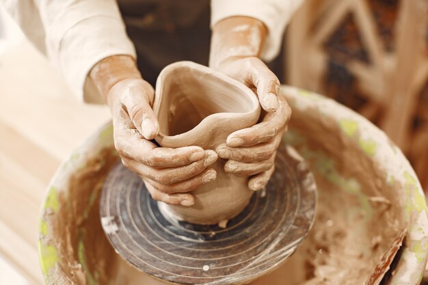 Potter femminile che lavora con l'argilla sulla ruota in studio. L'argilla con l'acqua schizzò intorno al tornio.