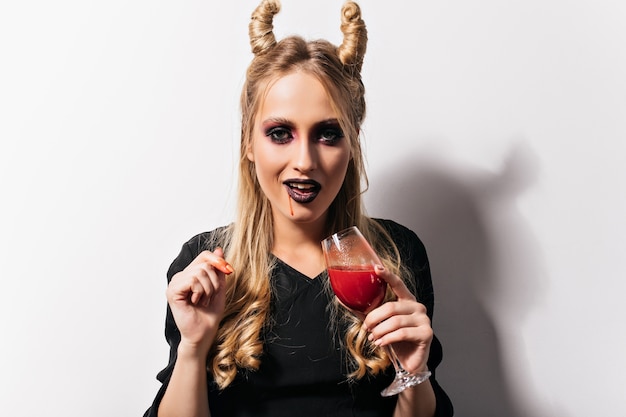 Pozione bevente della strega bianca soddisfatta in halloween. Vampiro giocoso che tiene il calice con il sangue.