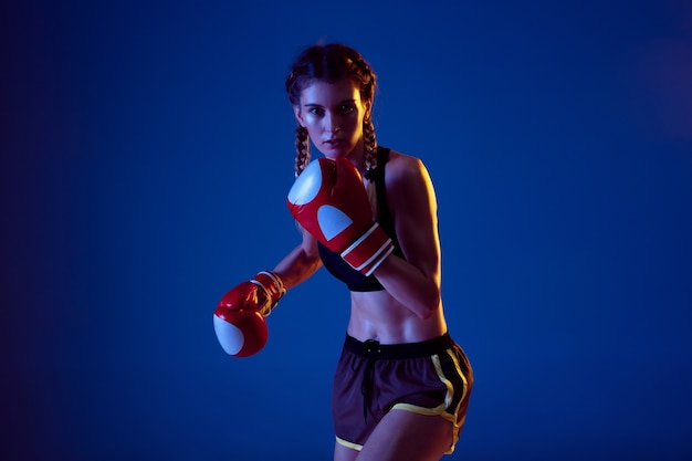 Pratica. Montare la donna caucasica nella boxe di abbigliamento sportivo su sfondo blu in luce al neon.