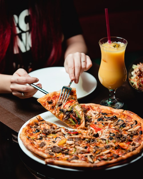 Prendendo una fetta di pizza mista con un bicchiere di succo d'arancia.