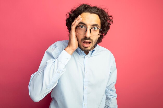 Preoccupato giovane uomo bello con gli occhiali mettendo la mano sulla testa guardando la parte anteriore isolata sul muro rosa