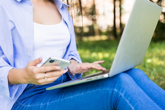 Pretty girl in blue jeans studi con laptop e telefono in citypark